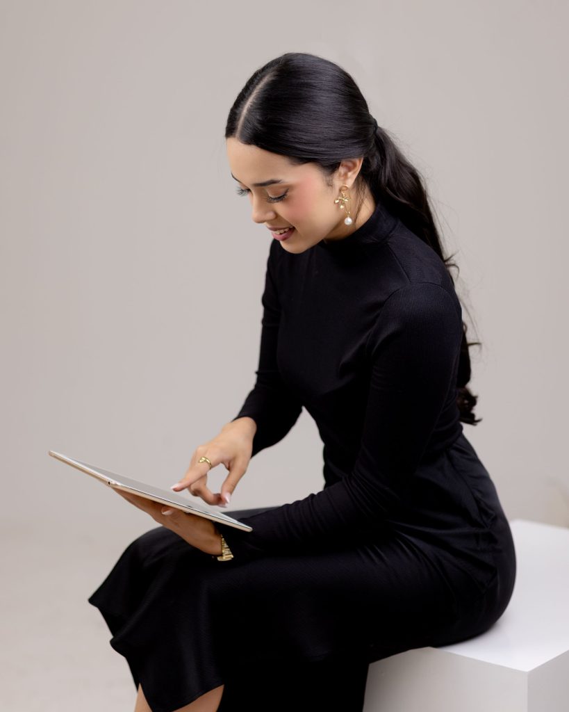 Fotografía de Adriana Castellón, fundadora de Alma Marketing Studio, con un vestido profesional negro realizando un trabajo de marketing en su tableta mientras está sentada.