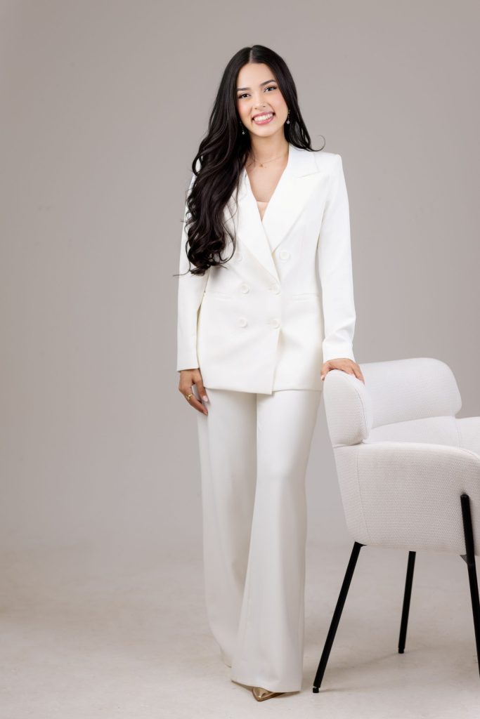 Fotografía de Adriana Castellón, fundadora de Alma Marketing Studio, con atuendo profesional, de pie mientras se sostiene de una silla.